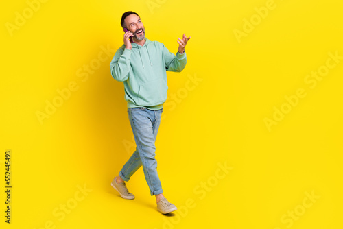 Full length photo of satisfied man walking street going looking empty space speaking friends 4g speed isolated on yellow color background