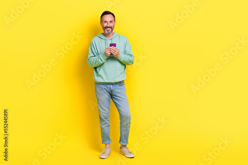 Full length photo of positive satisfied man use quality gadget stand empty space cool offer discount isolated on yellow color background