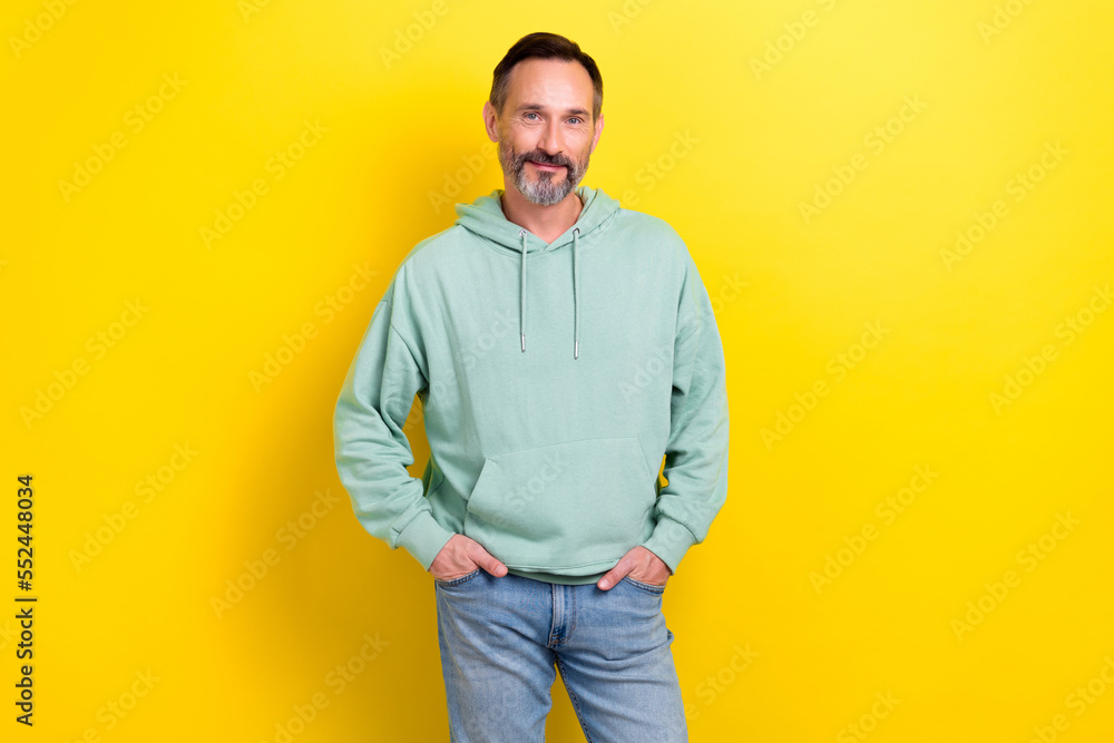 Photo of smiling cheerful middle mature man wear khaki sweatshirt hands pockets look you advert new clothes brand isolated on yellow color background Photo of smiling cheerful middle mature man wear khaki sweatshirt hands pockets look you advert new clothes brand isolated on yellow color background