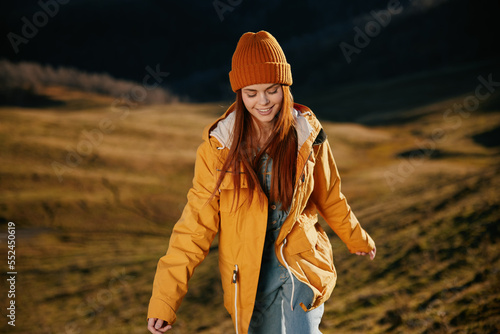 Woman running up the hill to the camera smile with teeth in the mountains in the autumn in a yellow raincoat and jeans happy sunset trip on a hike mountains in the snow, freedom lifestyle  © SHOTPRIME STUDIO
