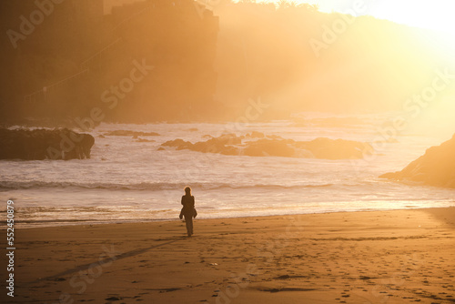 Silhouette of a woman on her back on the shore of a beach watching the sunset.