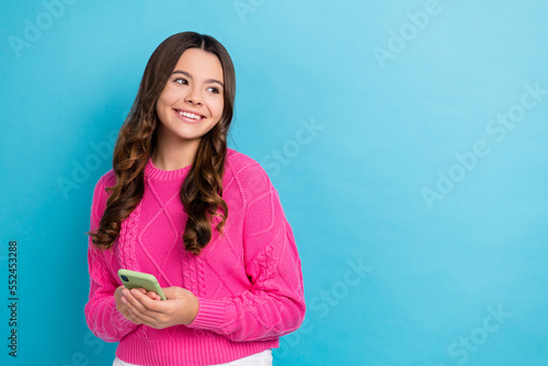 Photo of young dreamy lovely schoolgirl teen aged hold apple iphone look curious empty space useful convenient app isolated on blue color background