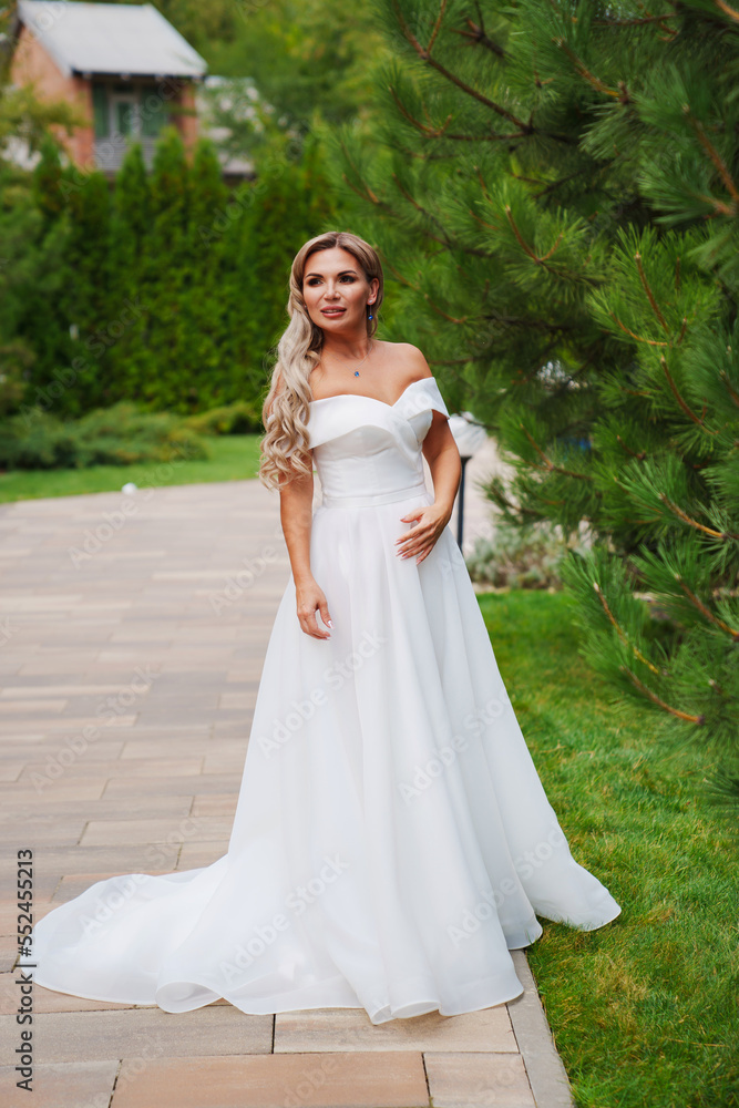 a blonde bride on a path in the park in a white long dress. a blonde bride on a path in the park in a white long dress.