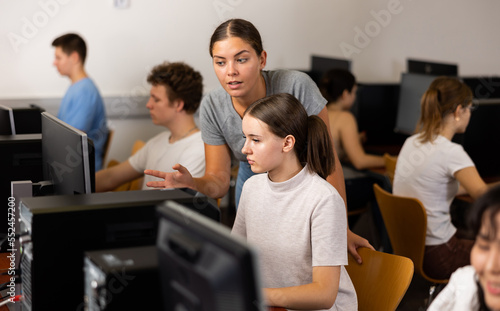 Young female teacher working with schoolgirl in computer class of school library