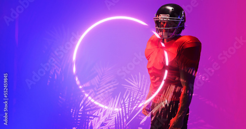 American football player wearing red uniform and helmet standing by illuminated circle and plants