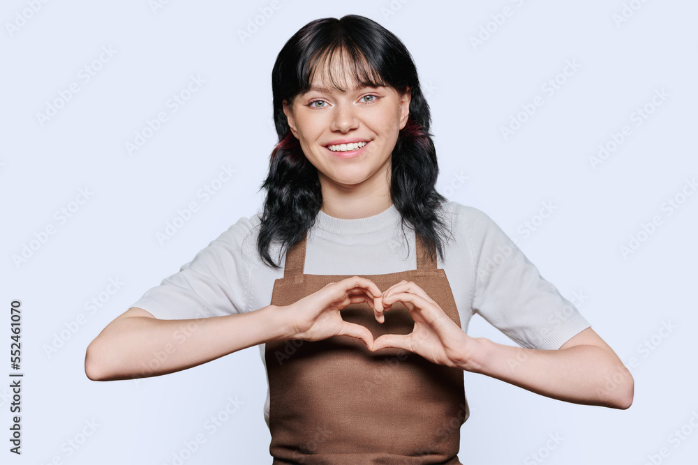 Smiling young female service worker in apron showing heart gesture, on white background Smiling young female service worker in apron showing heart gesture, on white background
