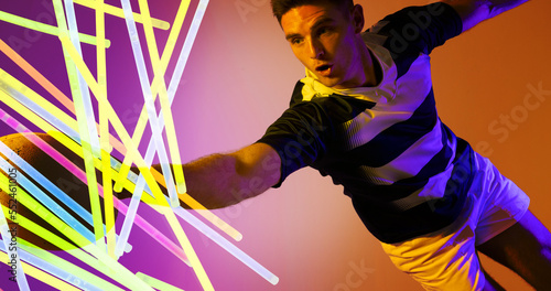 Caucasian rugby player jumping and catching ball by colorful glowing lines on colored background