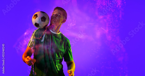 Caucasian soccer player practicing with ball and abstract design over blue background, copy space