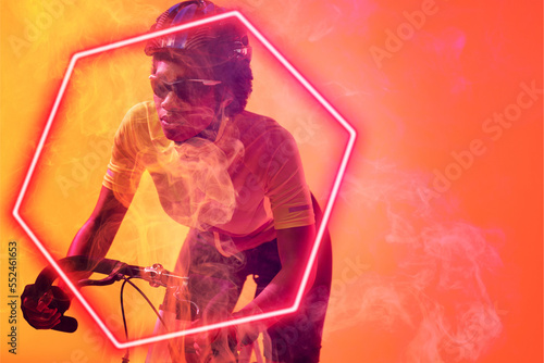 Hexagon neon over dedicated african american cyclist riding bicycle against orange background