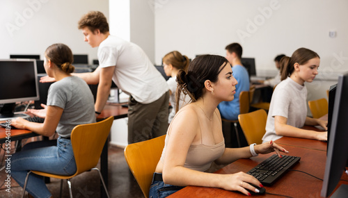 Interested teen girl studying with classmates in school computer class