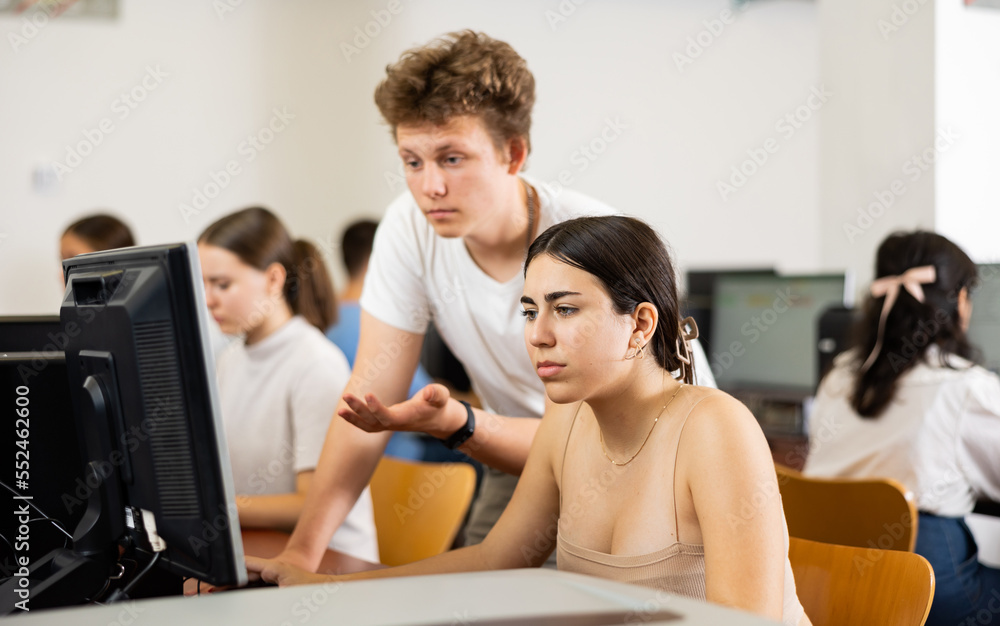 Fototapeta premium Teenagers using computer during computer science lesson in classroom. Boy and girl solving task together.
