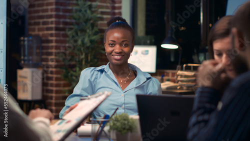 African american businesswoman smiling portrait in business meeting  coworkers talking in boardroom  slow motion. Diverse colleagues  woman looking at camera  slow motion medium shot. Handheld shot.