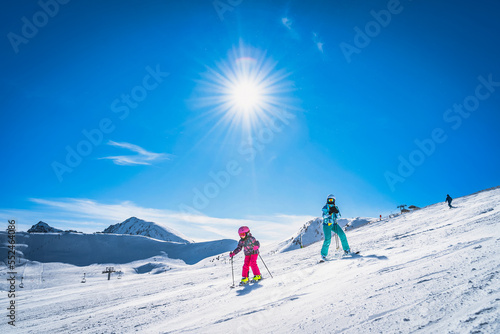 Mother teaching daughter how to ski, skiing down on a ski slope. Sunny day on ski winter holidays in Andorra, El Tarter, Pyrenees Mountains
