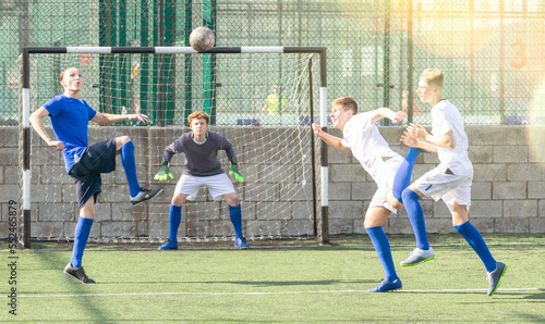 Game moments of football match between two teams of teenagers in white and blue shirts