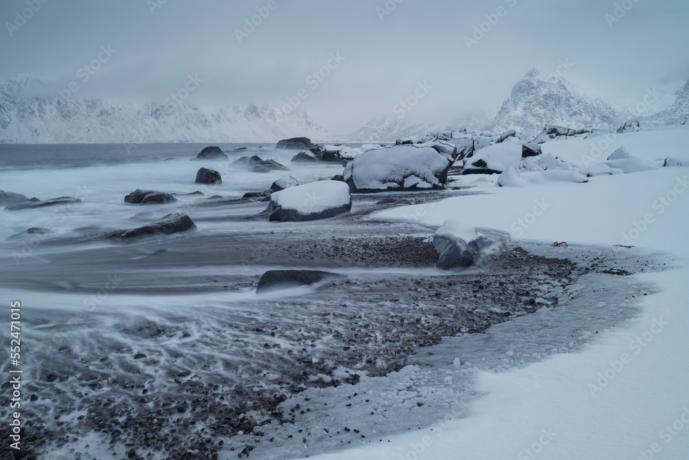 Waves recede from rocky snow covered beach, Lofoten Islands, Norway