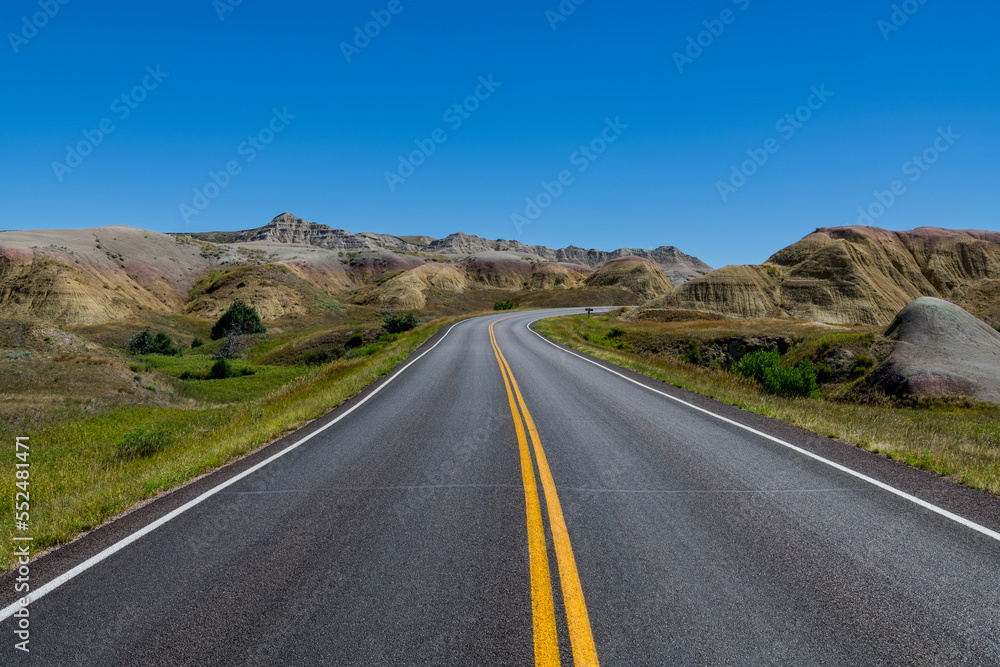 Highway curves through landscape of grassland and colorful peaks in Badlands National Park
