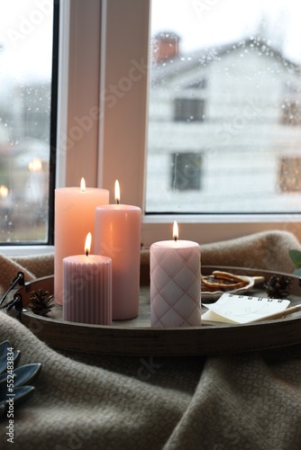 Tray with burning wax candles and decor on window sill indoors