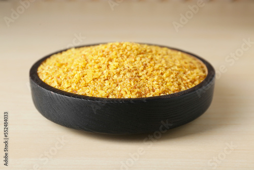 Bowl of uncooked bulgur on wooden table, closeup view