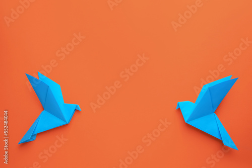 Beautiful light blue origami birds on orange background, flat lay. Space for text