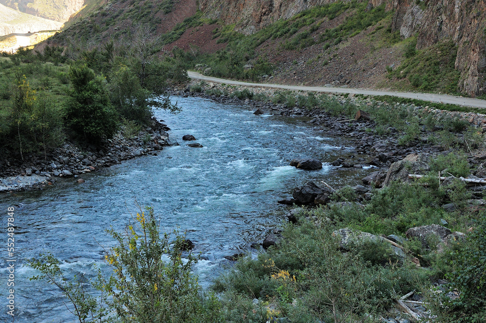 A stormy stream of a small mountain river flowing along the bottom of the canyon in the shadow of the setting sun. A stormy stream of a small mountain river flowing along the bottom of the canyon in the shadow of the setting sun.