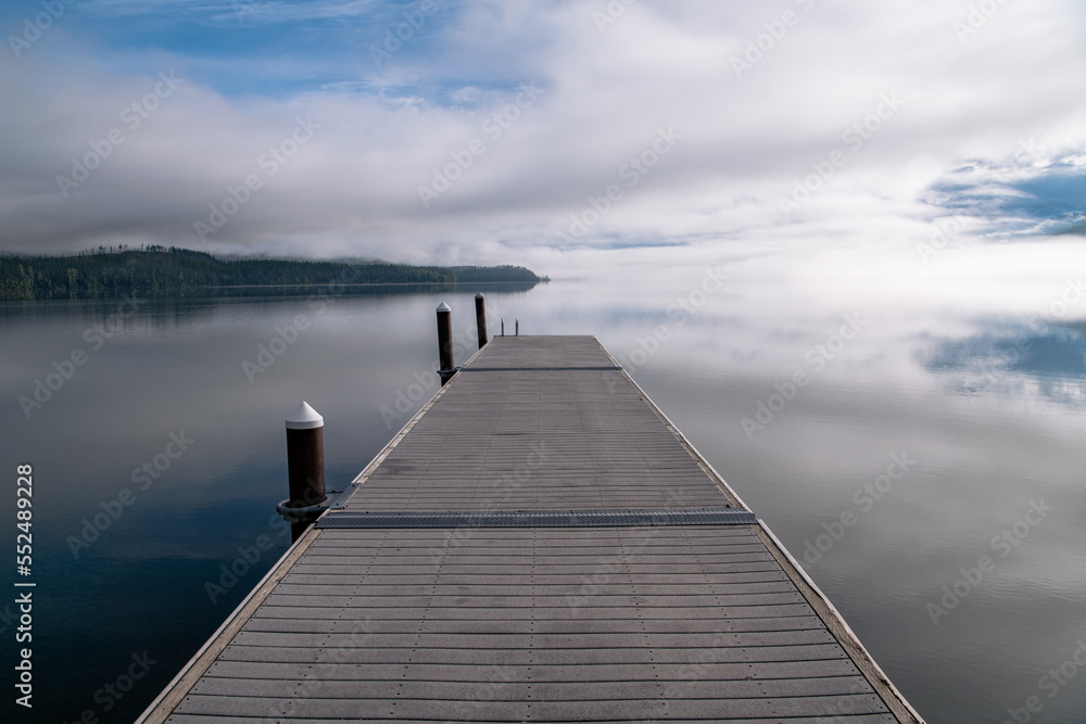 Perspective view of boat dock over tranquil lake reflecting blue sky, clouds, and fog at Lake McDonald, Glacier National Park, Montana