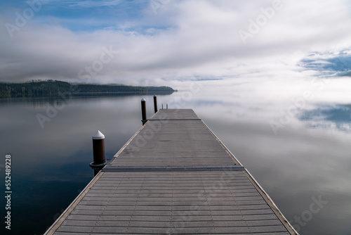 Perspective view of boat dock over tranquil lake reflecting blue sky, clouds, and fog at Lake McDonald, Glacier National Park, Montana