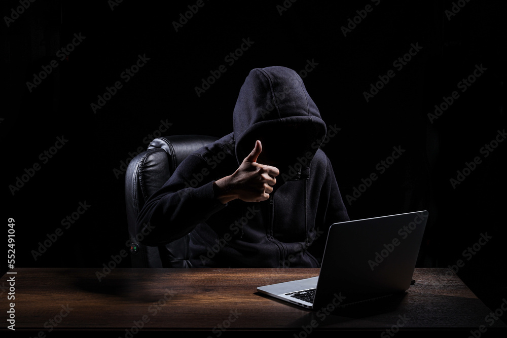 A hacker, dressed in a black hood, is raising a thumbs up when completing tasks to hack into a darkened room. A hacker, dressed in a black hood, is raising a thumbs up when completing tasks to hack into a darkened room.