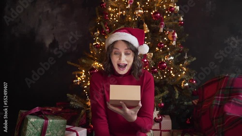A young beautiful woman is opening a gift box, light shines on her face. 