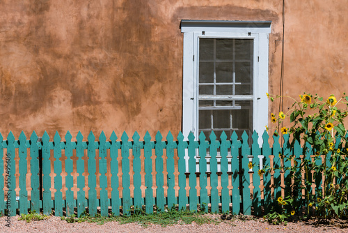 Sunflowers and turquoise color wood fence set in front of a window and old adobe wall along Canyon Road in Santa Fe, New Mexico photo