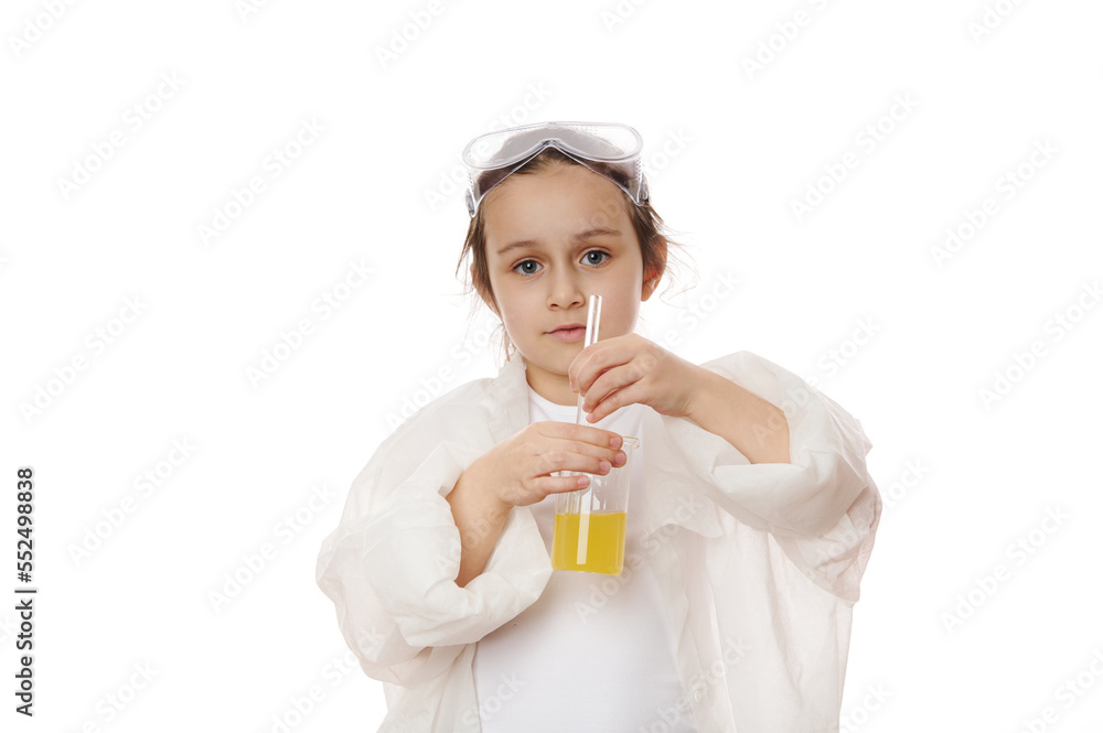 Smart primary school student, little girl in lab coat, using laboratory glass stick, mixes yellow chemical solution in beaker, shows the ongoing chemical reaction, looking at camera, white background Smart primary school student, little girl in lab coat, using laboratory glass stick, mixes yellow chemical solution in beaker, shows the ongoing chemical reaction, looking at camera, white background
