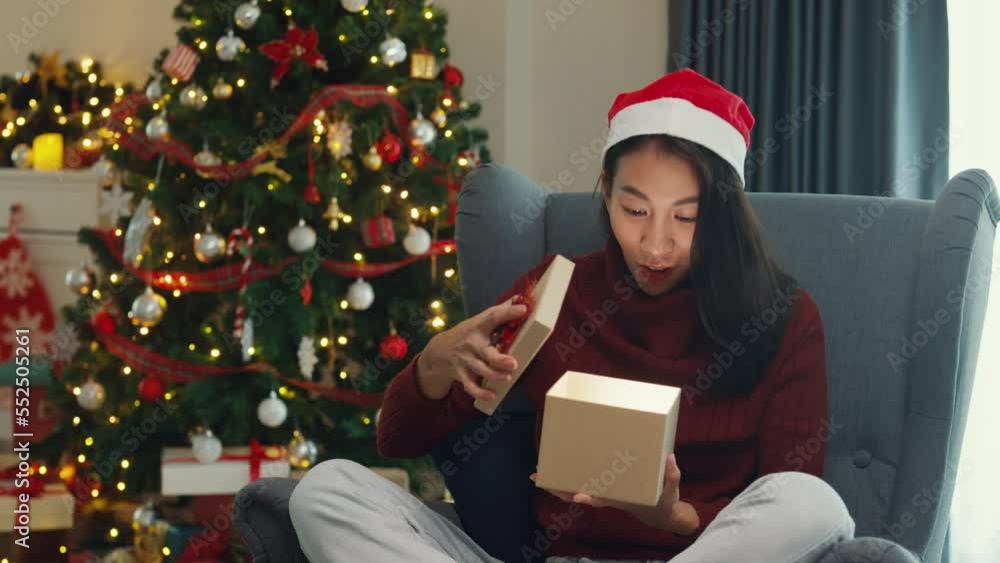 Surprise excited Asia female wear red sweater new normal celebrate christmas eve unboxing online shopping present gift delivery from friend and family on wing chair in living room at house. Surprise excited Asia female wear red sweater new normal celebrate christmas eve unboxing online shopping present gift delivery from friend and family on wing chair in living room at house.