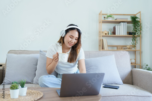 asian teenage girl using computer and wearing headphones at sofa