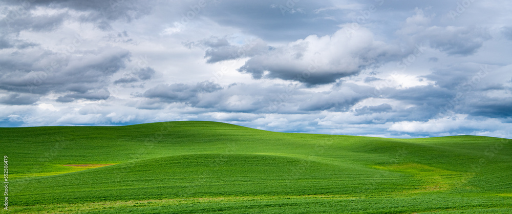 Panorama landscape of a countryside of idyllic green hills illuminated by breaks in the clouds of a dramatic sky