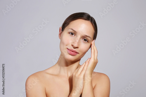 Studio portrait of young beautiful woman with long black hair tied in ponytail touching her face. Close up, copy space, isolated gray background.