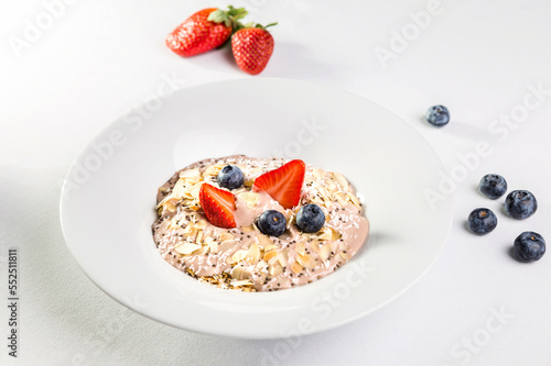 Oatmeal with almonds, blueberries and strawberries in a white plate on a white background