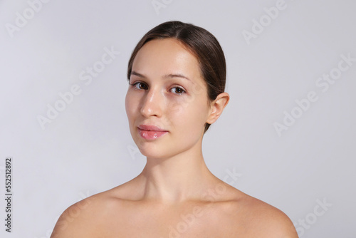 Studio portrait of young beautiful woman with long black hair tied in ponytail and clean face skin. Close up, copy space, isolated gray background.