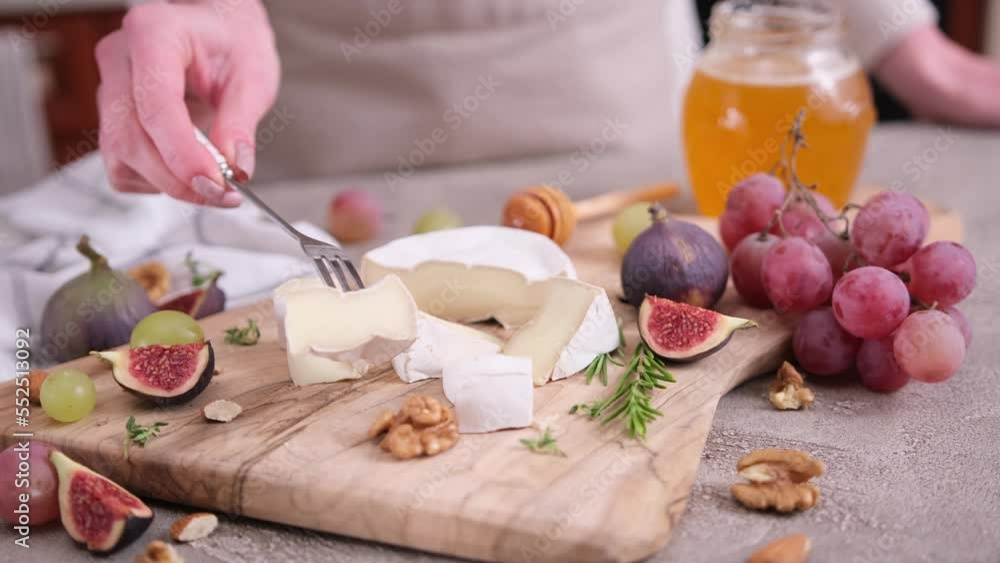 Woman puts on a fork piece of Camembert or brie cheese at domestic kitchen Woman puts on a fork piece of Camembert or brie cheese at domestic kitchen