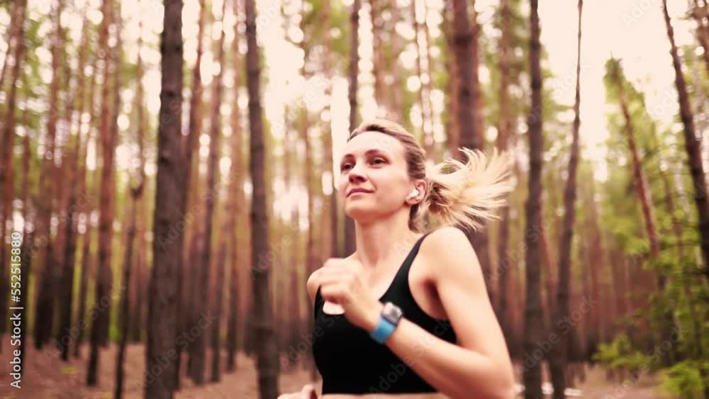 Beauty blonde girl running in forest while wearing fitness clothes and headphones. 4k. Slow motion Beauty blonde girl running in forest while wearing fitness clothes and headphones. 4k. Slow motion
