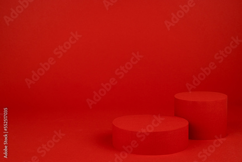 Two red cylinder podiums mockup on table on rich saturated background for presentation cosmetic products, gifts, goods in elegant minimal modern style, copy space. Template for advertising, design.