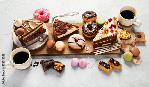 Table with various cakes, cookies, donuts and coffe cups on light background.