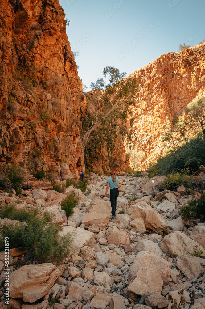 Atemberaubender Olive Trail - Mädchen wandert durch eine enge, felsige Schlucht mit rot leuchtenden Felswänden, Naukluft Gebirge, Namibia Atemberaubender Olive Trail - Mädchen wandert durch eine enge, felsige Schlucht mit rot leuchtenden Felswänden, Naukluft Gebirge, Namibia