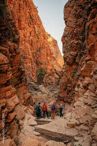 Atemberaubender Olive Trail - Familie wandert durch eine enge, felsige Schlucht mit rot leuchtenden Felswänden, Naukluft Gebirge, Namibia