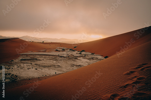 Blick von der Düne Big Daddy in ein Vlei mit seinem weißen rissigen Ton-Schluff - die aufgehende Sonne durchflutete den Morgennebel und sorgt für eine magische Lichtstimmung, Sossusvlei, Namibia photo