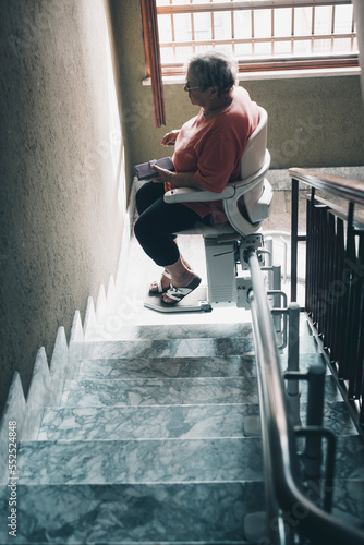 One old woman with legs problems use electric engine chair to up the stairs at home in a building. Tecnology to help elderly life for people concept photo