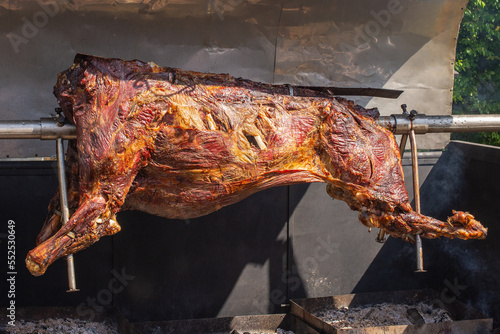 The whole bull grilled traditionally with coal and fire. Roasted bull on the metal spit. Outdoor restaurant with a giant bull that is cooking on a skewer photo