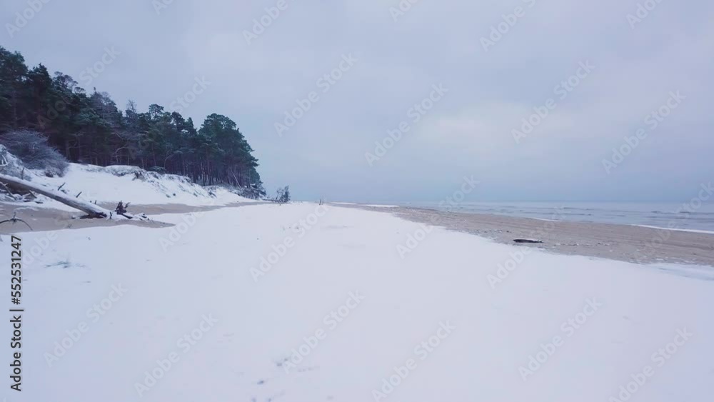 Beautiful aerial view of Baltic sea coast on a overcast winter day, beach with white sand covered by snow, coastal erosion, climate changes, wide angle drone shot moving backward low Beautiful aerial view of Baltic sea coast on a overcast winter day, beach with white sand covered by snow, coastal erosion, climate changes, wide angle drone shot moving backward low