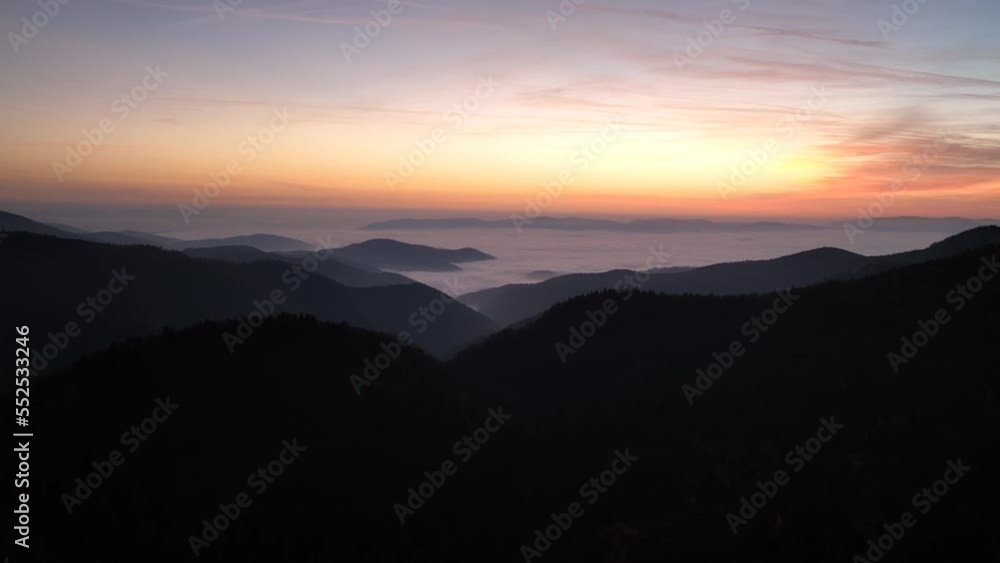 Aerial cinematic scene with a sunset above the mountains covered in fog Aerial cinematic scene with a sunset above the mountains covered in fog