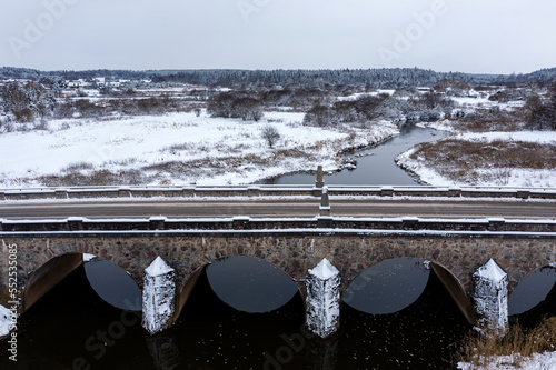 An old stone bridge with arches over the Abava river on a snowy winter day, Kandava, Latvia photo