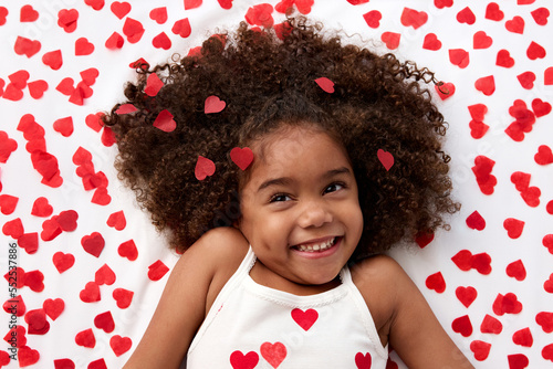 Happy young girl with afro hair giggling on bed surrounded by heart shaped confetti