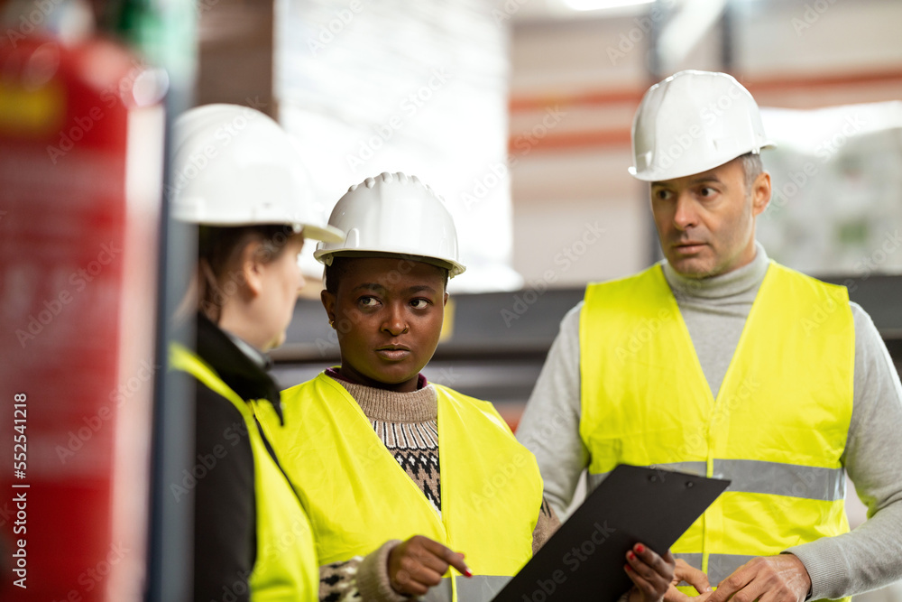 A multiracial group of people is working in a distribution warehouse, the manager is giving instructions to the workers. A multiracial group of people is working in a distribution warehouse, the manager is giving instructions to the workers.